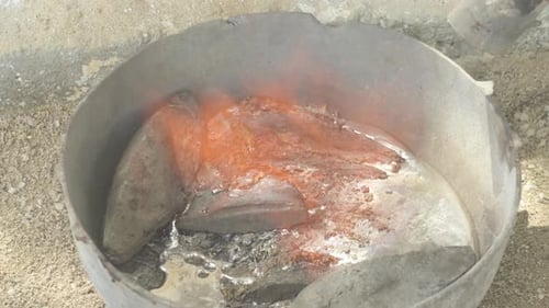 Molten lead in a metal container with fumes rising, industrial setting, close up