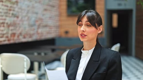 Confident Businesswoman Expresses Positive Emotions in Modern Office Cafe with Documents