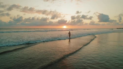 Woman walking on wet sand beach at sunset along calm ocean waves in Costa Rica