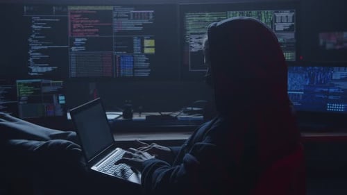 A Hacker Works Intently in a Dim Room Surrounded By Gadgets