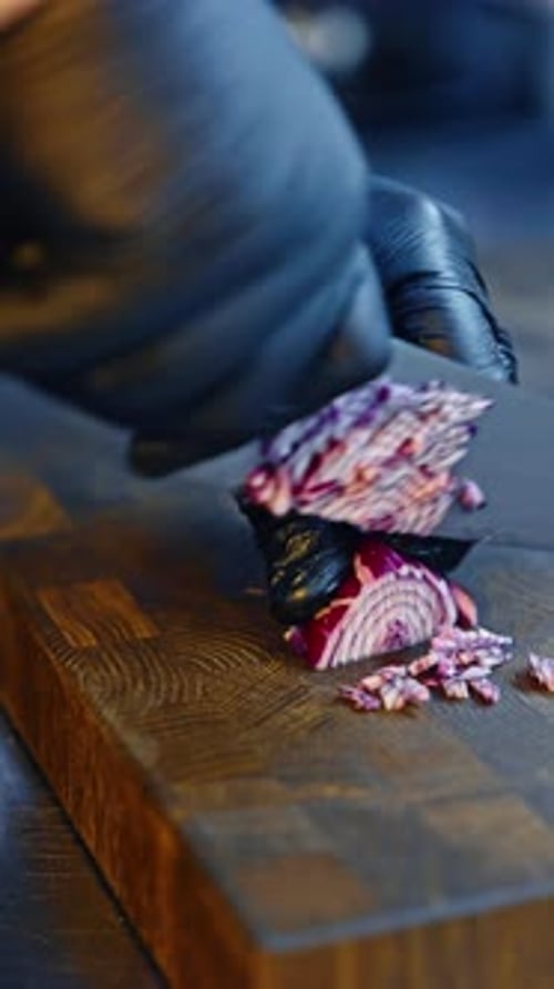 Chef cutting onions with a big knife on the wooden board. Preparing vegetables in the restaurant.