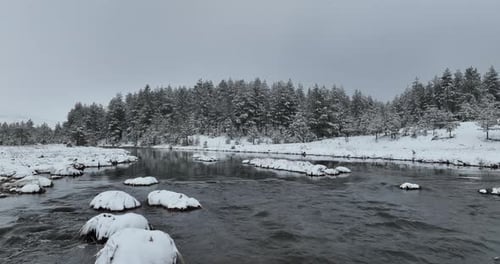 An Aerial View of a Frozen River Flowing Through Snowcovered Forests on a Cloudy Sunset Sky