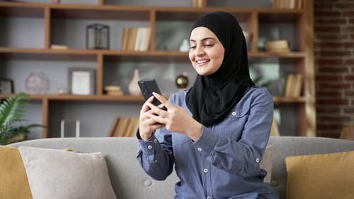 Smiling Woman Uses Smartphone on Sofa Indoors