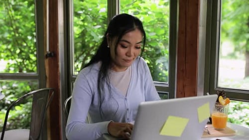 Young Asian woman working in coffee shop using laptop.
