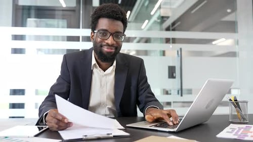 Portrait of a happy African American businessman sitting at workplace in business office. Head shot