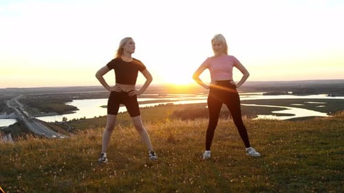 Two Young Sportive Woman Standing on the Field at Sunset and Warming Up Their Bodies Make Circular