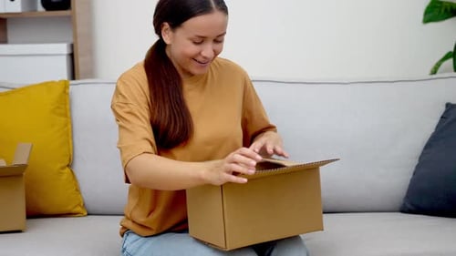 Woman Sitting on Couch Opening a Cardboard Box