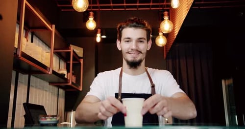 Smiling Man Behind Counter Offers Coffee Drink