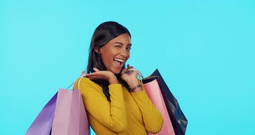 Happy woman, shopping bags and wink in studio for purchase, sale or discount against a blue