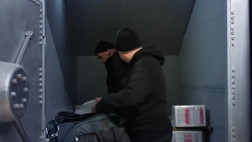 Bank robbers on a heist loading bundles of cash into a bag and escaping out of a bank vault