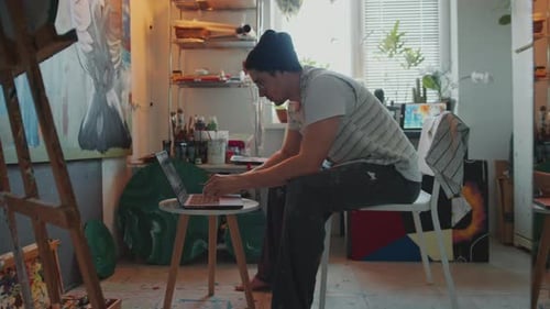 Professional Painter Using Laptop during Workday in Creative Studio