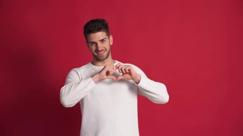Young Adult Making Heart Shapes on Red Background