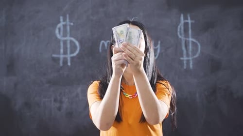 Woman writing Money on blackboard looks at camera with happiness.