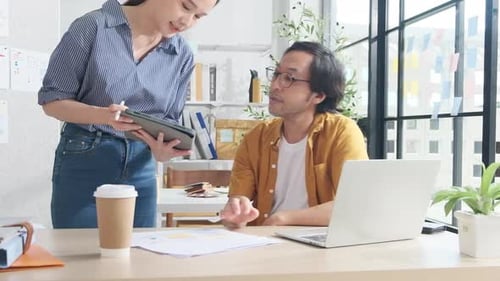 Two young Asian startup partners are working in a casual small business office.