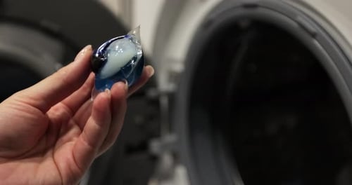 Close Up Woman Puts Colorful Gel Capsules with Laundry Detergent in the Washing Machine on Dirty