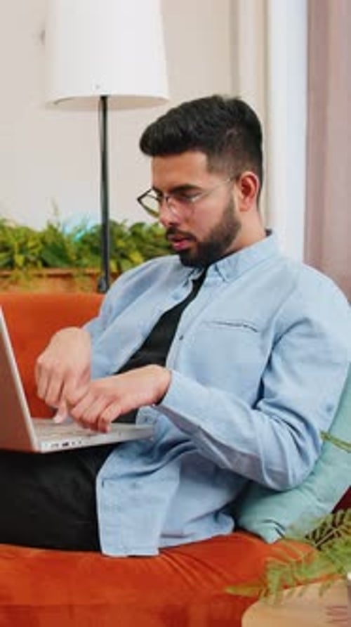 Man working on laptop on orange couch indoors