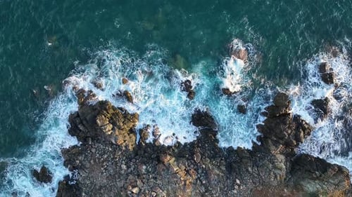 Waves crashing on rocky shore at coastal location during sunset