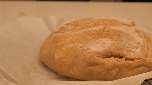 Pfanne in Zeitlupe rund um den vollen, frisch gebackenen Laib Sauerteigbrot, belegt mit Mehl, das auf dem Kitc liegt