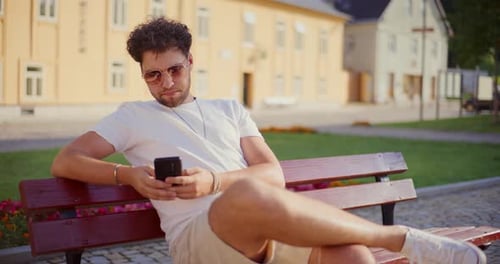 Young Man Relaxing with Phone on Park Bench