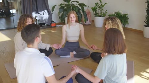 Group Meditating Holding Hands in Bright Indoor Studio