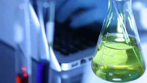 Laboratory Beaker with Yellow Liquid and Laptop