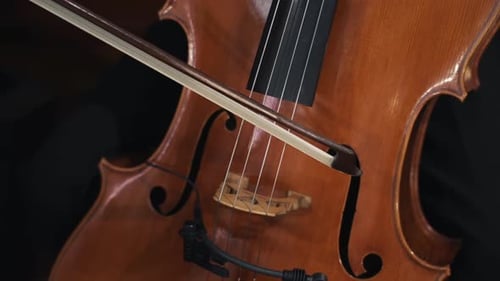 Close-up of a musician playing a cello with a bow, highlighting the strings and wooden body.