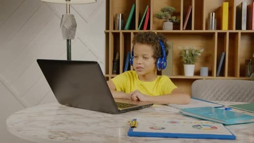 Cute Preadolescent Black Boy in Headphones Elearning with Laptop at Home