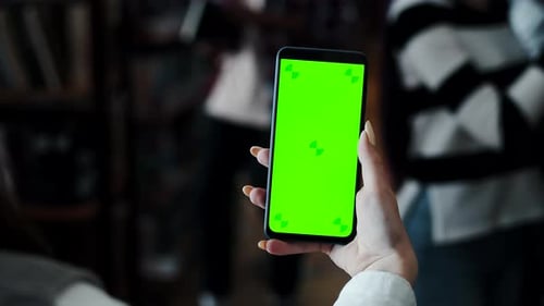 Woman Holding Smartphone in Hand with the Mockup Green Screen Showing Copy Space in the Library