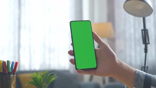 Close up of man's hand holding a mock up green screen smartphone on a desk