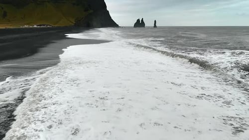 Wide foamy white waves arrive to the beach with black volcanic sand.
