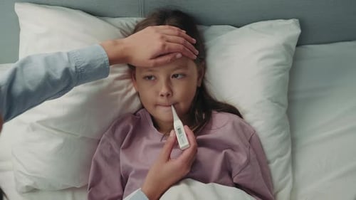 Sick Child Lying in Bed with Thermometer