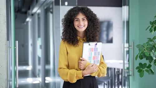 Portrait of a young smiling businesswoman standing in a business office with a folder in her hands.