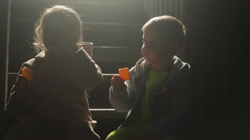 Two Children Eating Snacks in Dark Urban Setting