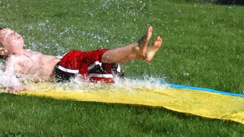 Boy Sledding on a Water Slide on Grass