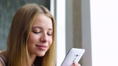Smiling woman looks at her phone in a bedroom