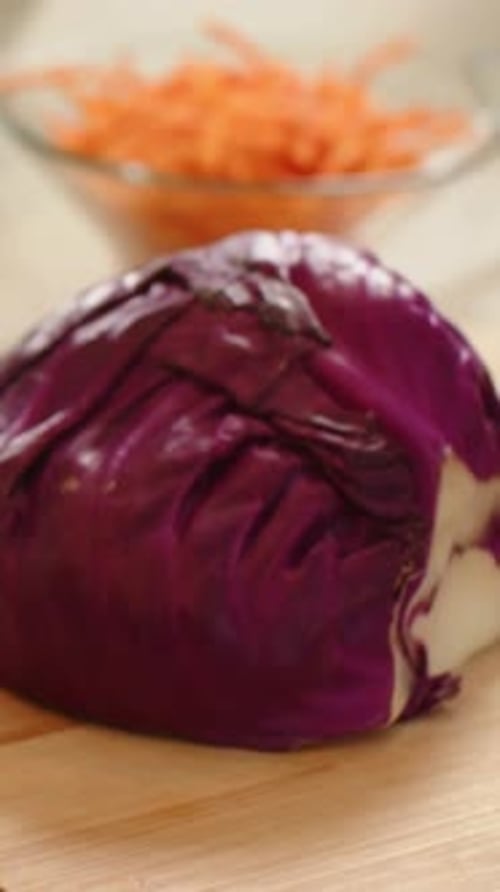 Vertical video: Pulling back camera from closeup on counter, showing half cabbage and carrot bowl