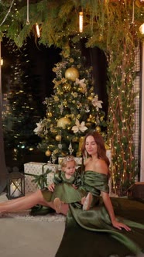 Mother and Daughter in Glamorous Dresses Sitting Near Decorated Christmas Tree New Year Celebration