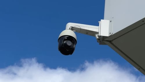 Modern surveillance camera mounted on a building against a blue sky.