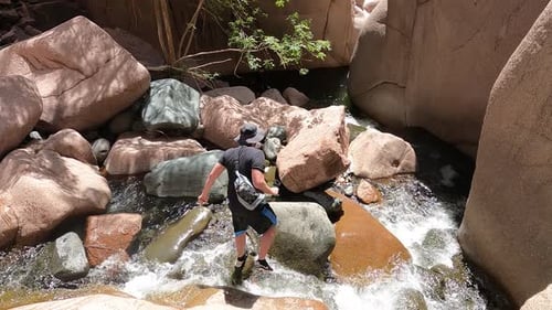 Man hiking a canyon filled with water in Arizona while stepping over rocks.