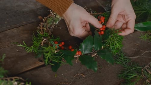 Hands Making Holiday Wreath With Berries and Greens