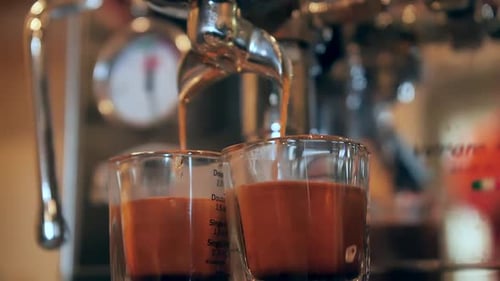 Espresso machine pouring coffee into two measuring cups, slow motion close up