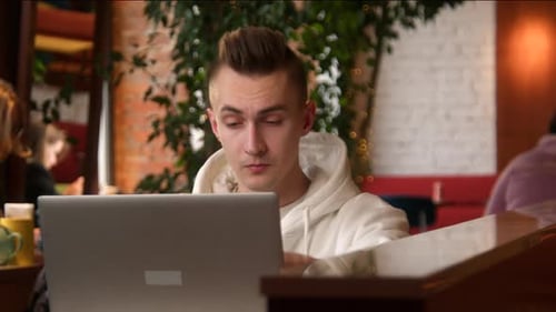Young Man is Concentrating on Laptop in Cafe Stock Footage Student is Writing Paper on Laptop in