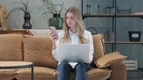 Woman Works on Couch with Laptop and Phone