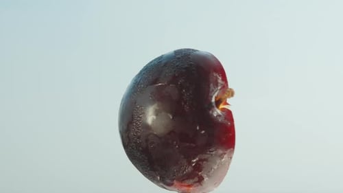 Half of a red plum swirling against the blue sky, close-up.