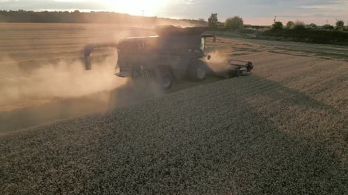 Low Drone Shot Behind Combine Harvester into the Sun at Sunset with Orange Dust at Sunset UK