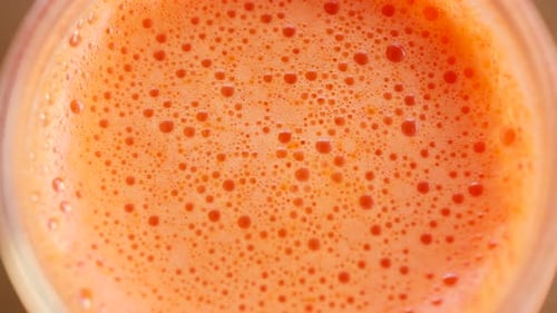Extreme close up of fresh orange juice surface with bubbles and foam texture