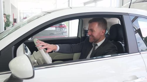 A Man Sits in a New Electric Car at a Dealership and Celebrates the Purchase of a New Car Buy a Car
