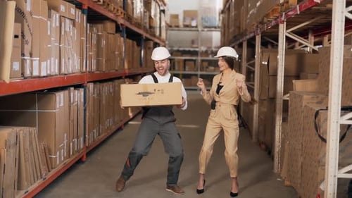 A man in a work uniform and a woman in a business suit happily dancing with a cardboard box