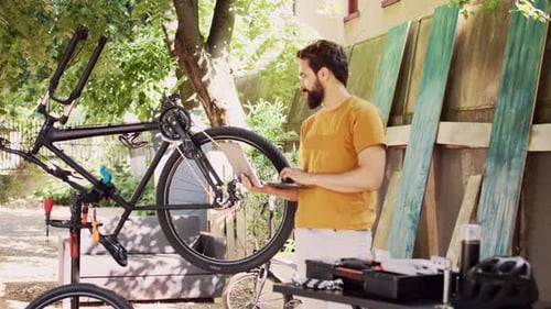 Man Upkeeping Bicycle with Laptop