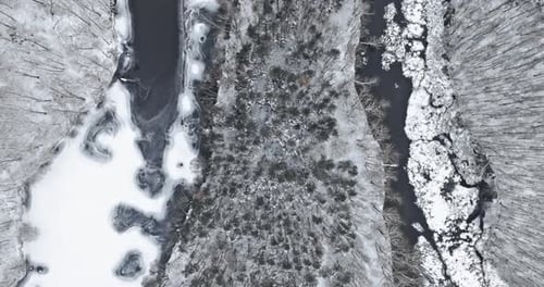 Aerial view of frozen river and snowy forest in winter.